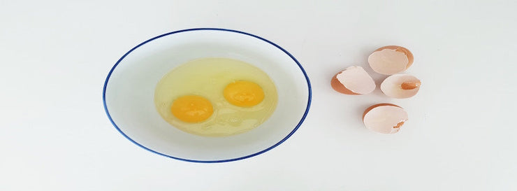 bowl containing two cracked eggs, alongside eggshells
