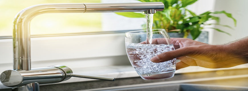 a hand holding a glass under a running kitchen tap