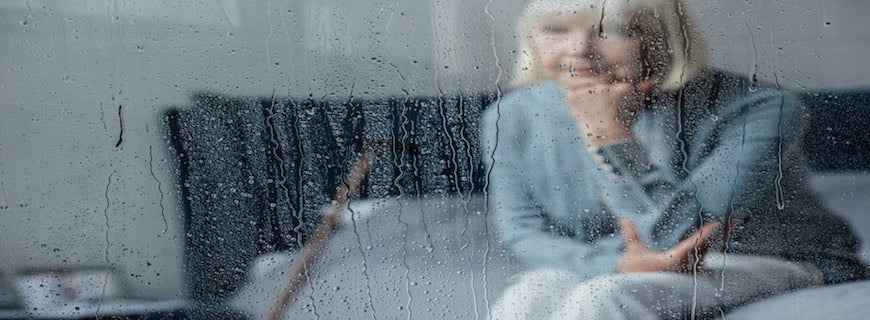 elderly woman surveying rain-streaked window from within house