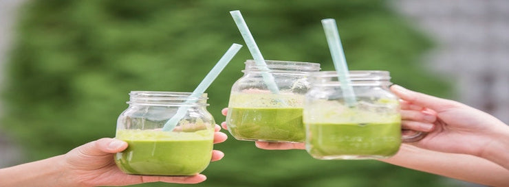 three green smoothies in glass jars being clinked by separate people