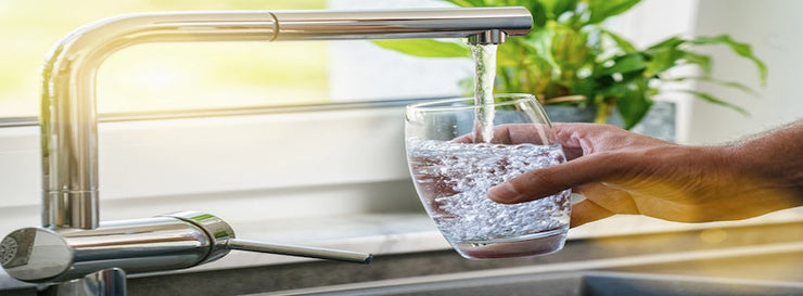 Hand holding a glass of water poured from the kitchen faucet