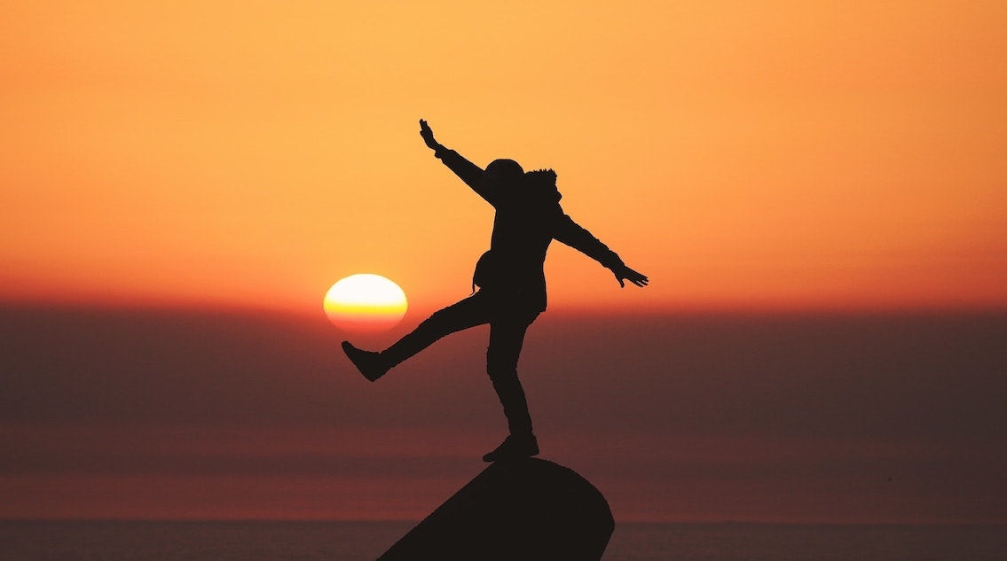 outline of person balancing on rock in sunset