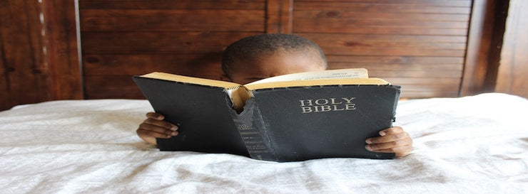 child's head appearing over the top of the Holy Bible, which he is reading
