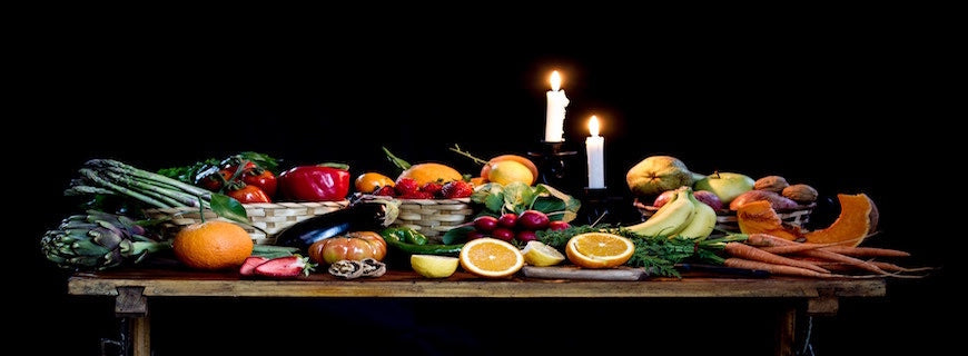 an array of colourful fruit and vegetables arranged on a candle-lit wooden table