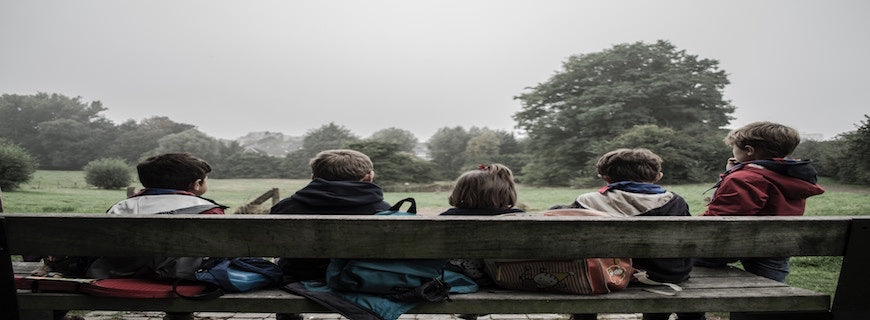 Five children with their backs to camera sitting on a park bench