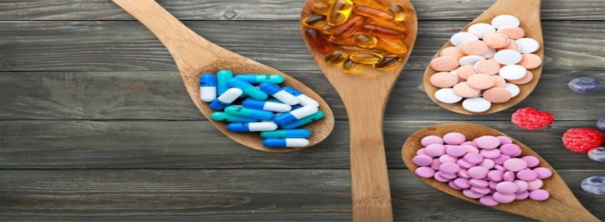 array of pills and capsules on wooden spoons