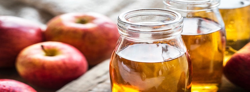 Jar of apple cider vinegar alongside some red apples