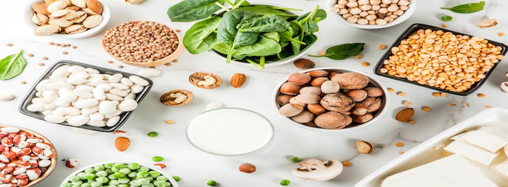 Array of vegan food, veggie protein sources: Tofu, vegan milk, beans, lentils, nuts, soy milk, spinach and seeds. Top view on white table.