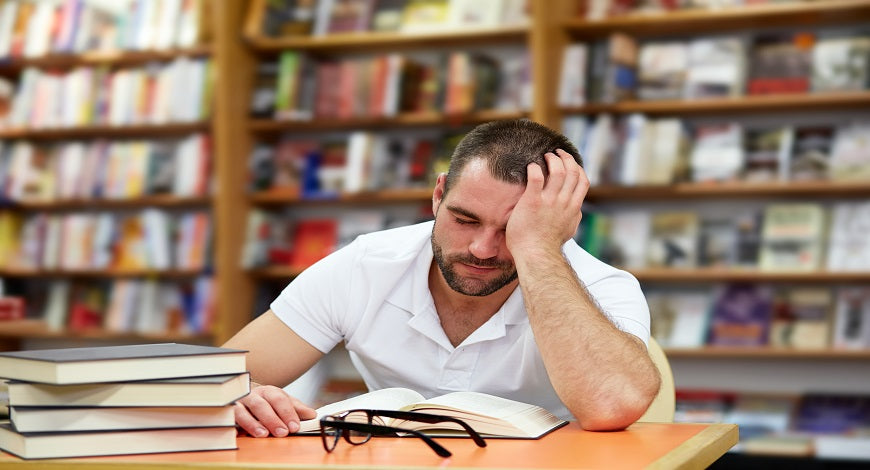 man at desk holding head in hand