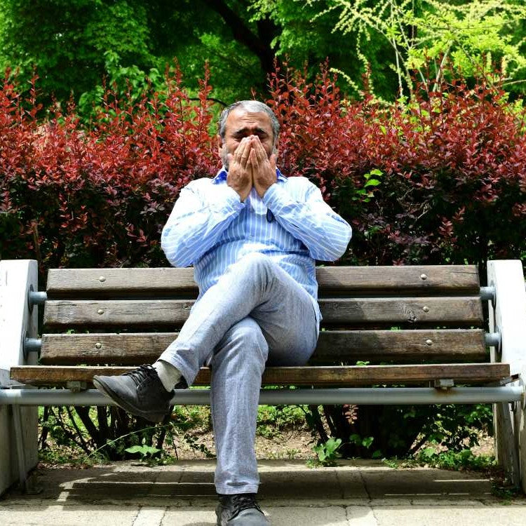 man sitting on bench sneezing